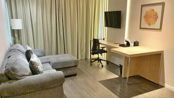 Uma sala de estar moderna com um sofá cinzento, uma escrivaninha de madeira e uma televisão.