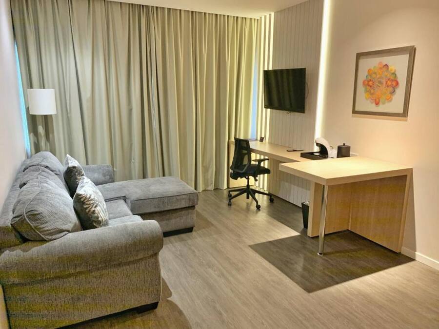 Uma sala de estar moderna com um sofá cinzento, uma escrivaninha de madeira e uma televisão.