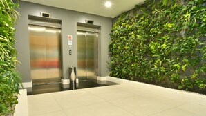 A modern elevator area with two elevators, a wall-mounted plant wall, and a tiled floor. - Holiday Inn Express Asuncion Aviadores by IHG (Asunción)
