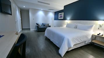 Ett hotellrum med en stor säng, ett skrivbord, en stol, en soffa och ett nattduksbord med en lampa.
