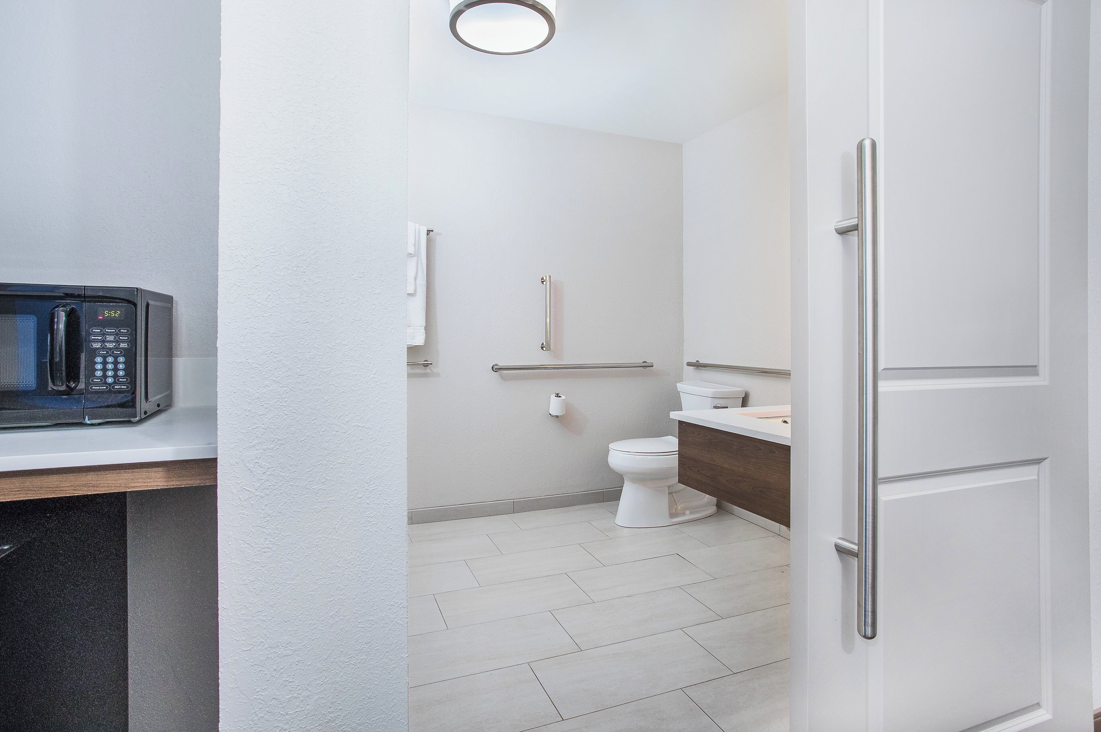 Un baño con inodoro y lavamanos blancos, un espejo y un microondas sobre la encimera.