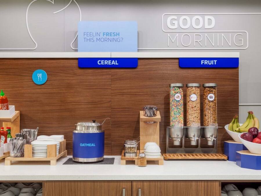 A breakfast bar with cereal and fruit options, a kettle, and condiments.