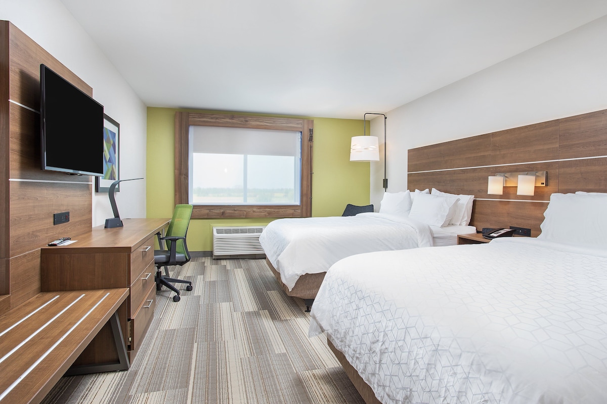 A hotel room with two beds, a desk with a chair, a TV, and a window.