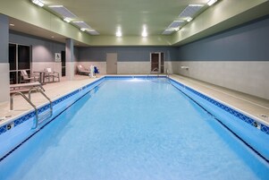Una piscina con borde de azulejos azules, una silla de salvavidas y una puerta a los vestuarios.