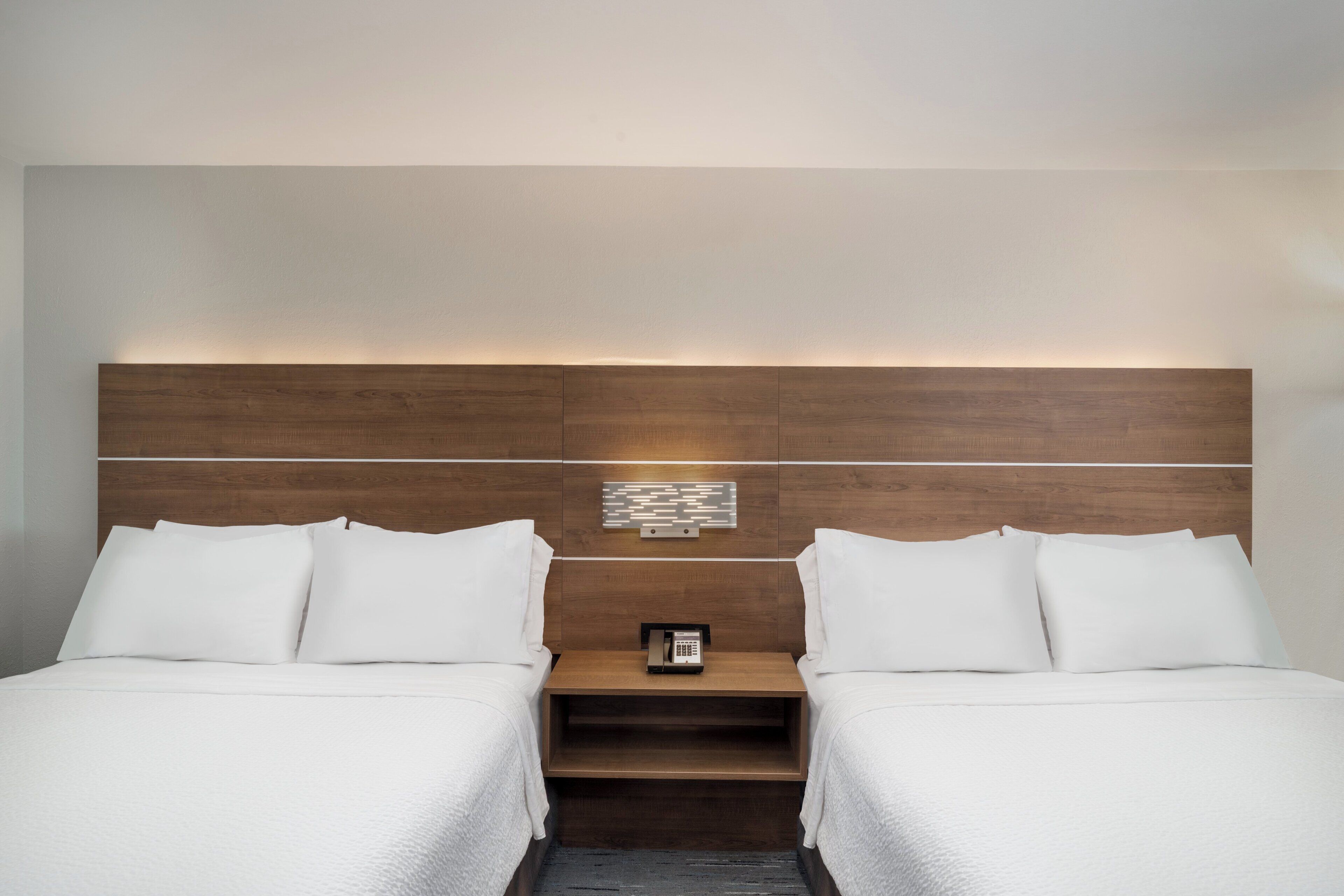 A hotel room with a double bed, a bedside table, a phone, and a wall-mounted light fixture.