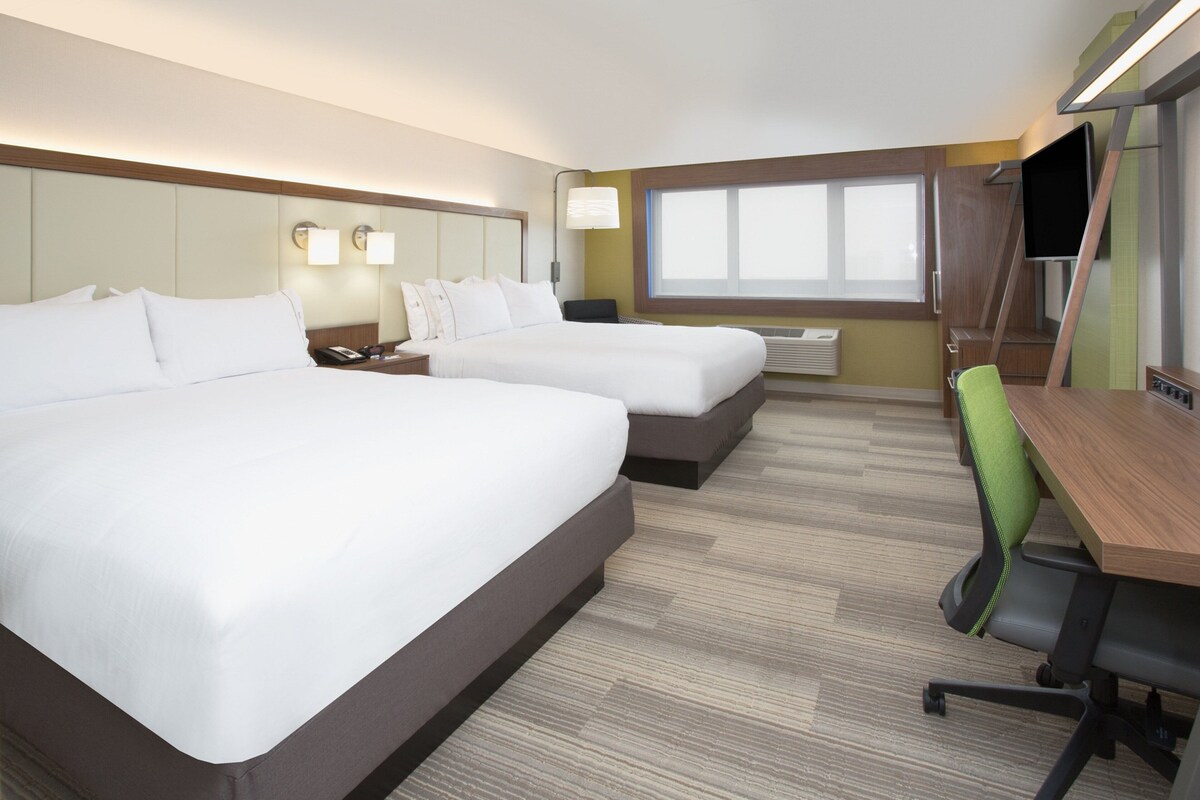A hotel room with two beds, a desk, a chair, a TV, and a window.