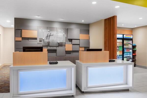 A hotel reception area with two reception desks, a wall-mounted sign, and a beverage refrigerator. - Holiday Inn Express and Suites Union Gap- Yakima Area by IHG (Yakima)