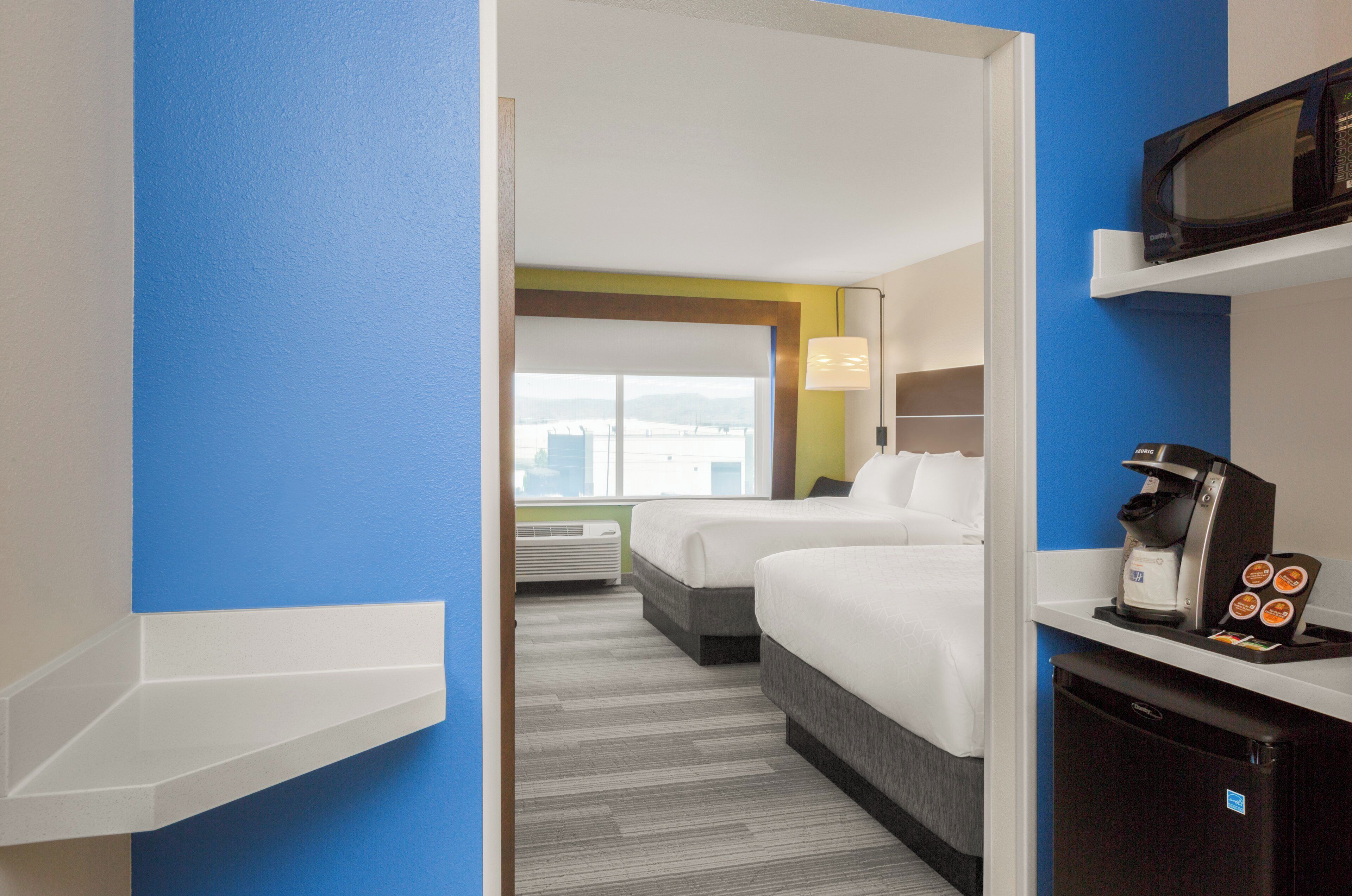 A hotel room with two beds, a microwave, a coffee machine, and a view of the city.