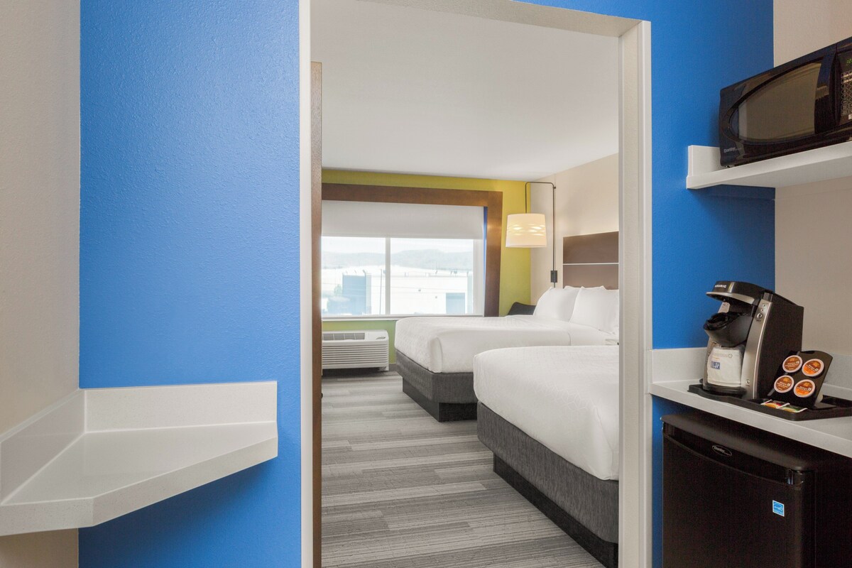A hotel room with two beds, a microwave, a coffee machine, and a view of the city.