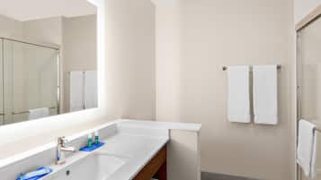 A modern bathroom with a large mirror, two sinks, and a shower area.