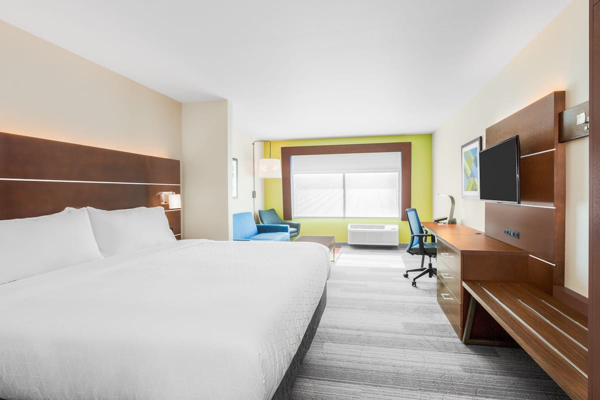 Ein Hotelzimmer mit einem großen Bett, einem Schreibtisch mit Computer, einem Sessel und einem Fernseher.