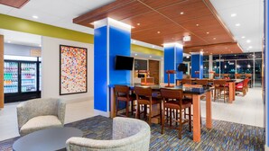 A modern hotel lobby with a seating area, a refrigerator stocked with beverages, and a large abstract painting on the wall. - Holiday Inn Express and Suites Union Gap- Yakima Area by IHG (Yakima)