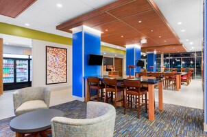Un moderno vestíbulo de hotel con zona de estar, un refrigerador lleno de bebidas y un cuadro abstracto grande en la pared.