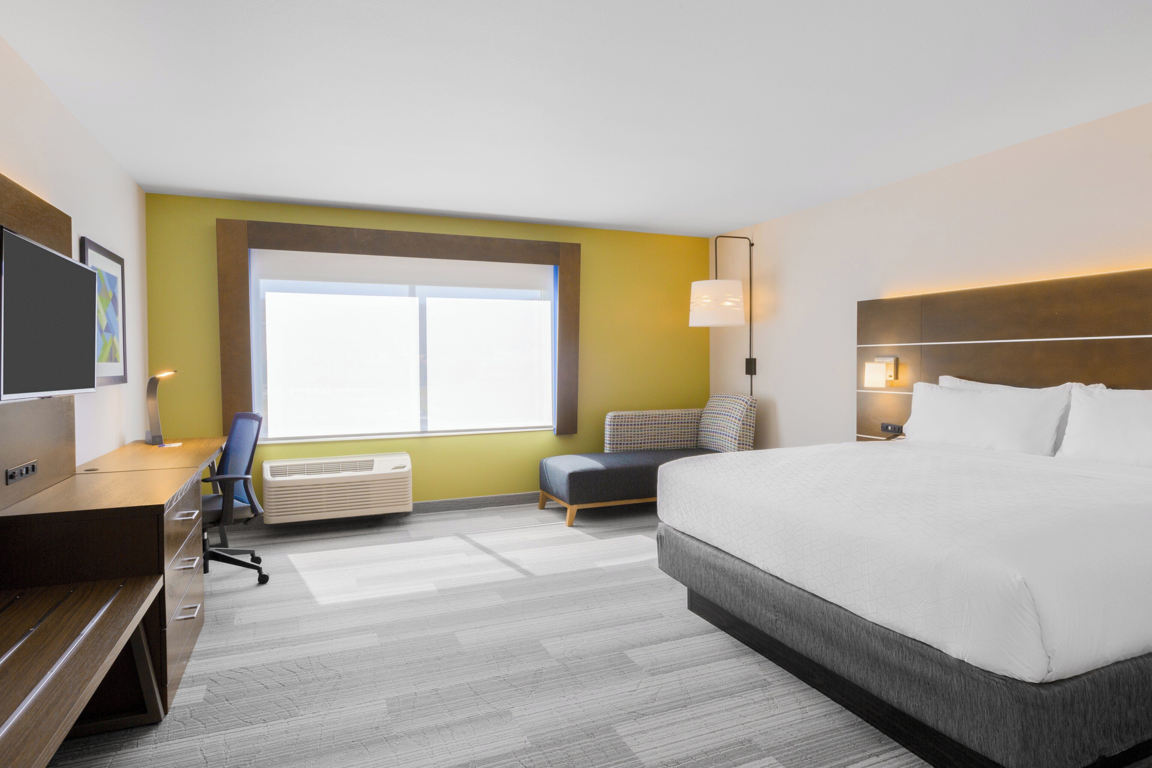 A hotel room with a bed, desk, chair, and a large window.