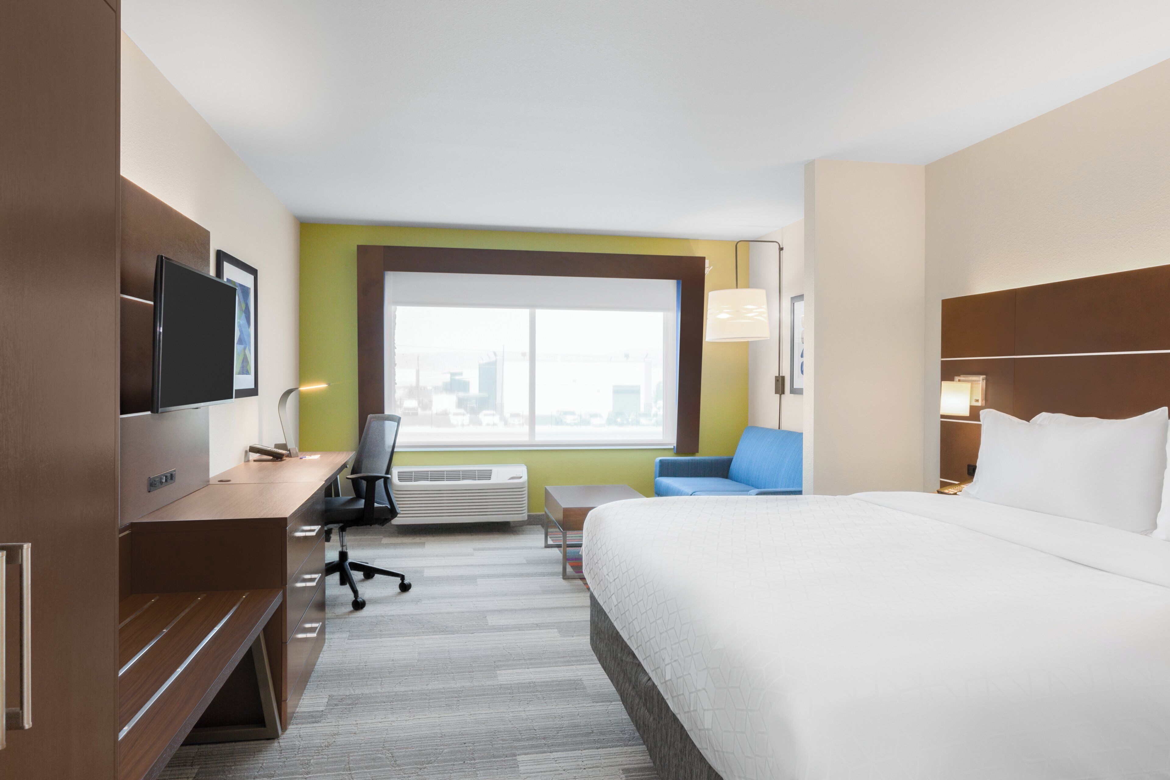 A hotel room with a bed, a desk, a chair, a television, and a window with a city view.