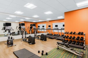 Un gimnasio con máquinas de cardio, bancos de pesas y mancuernas.