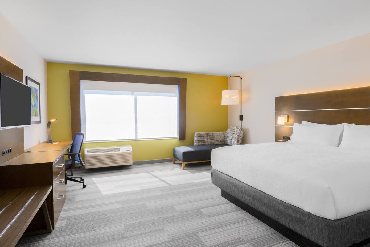 Ein Hotelzimmer mit Bett, Schreibtisch, Stuhl, Fernseher, Fenster und einer Wandlampe.