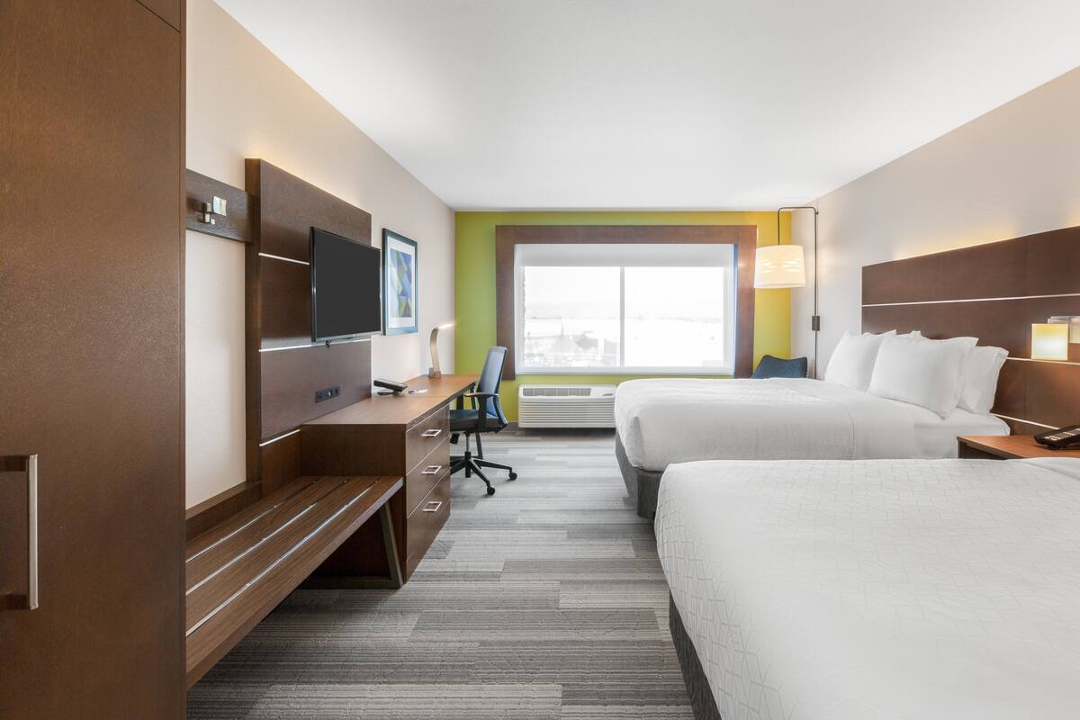 Ein Hotelzimmer mit zwei Betten, einem Schreibtisch mit Stuhl, einem Fernseher und einem Fenster mit Blick.