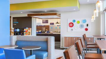 Un café moderne avec différents types de sièges, notamment des banquettes et des tables, un comptoir bien visible où est affiché le menu, et un mur décoré d’assiettes.