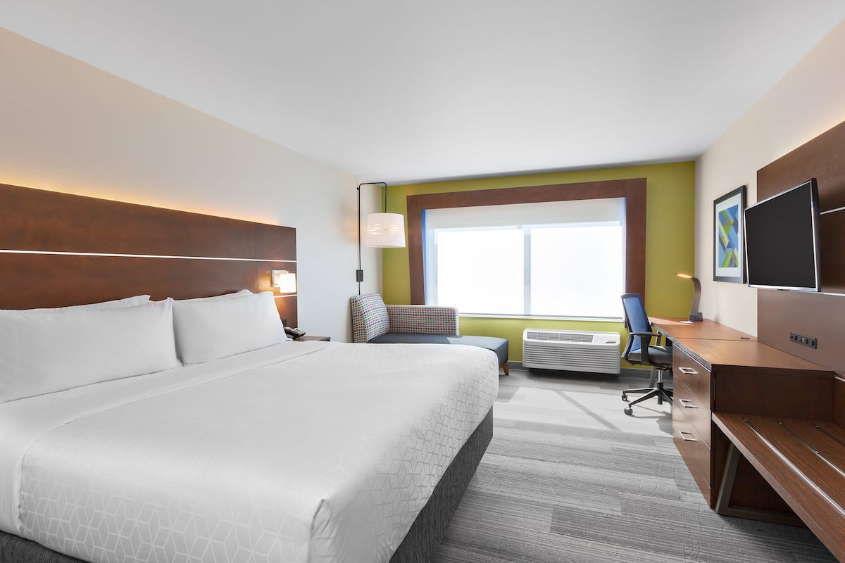 Ein Hotelzimmer mit einem großen Bett, einem Schreibtisch, einem Sessel, einem Fernseher und einem Fenster mit Blick.