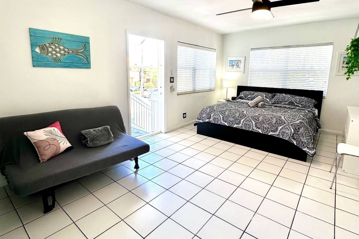 A bedroom with a bed, a sofa, a ceiling fan, and a window with blinds.