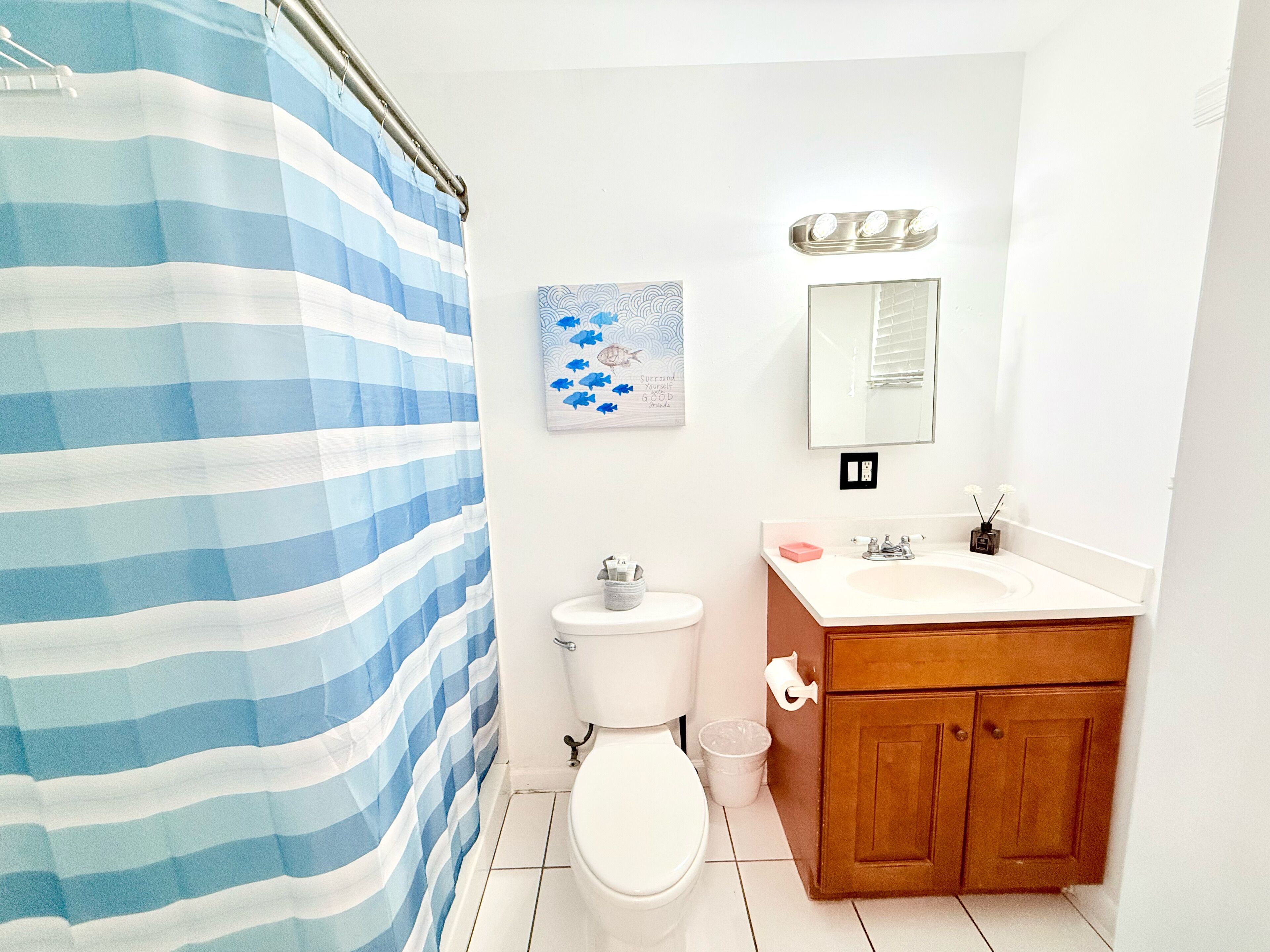 Une salle de bain avec un rideau de douche à rayures, des toilettes, un lavabo avec un miroir au-dessus, et un petit objet décoratif posé sur le lavabo.