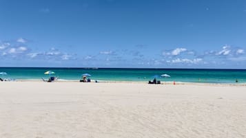 På stranden, hvidt sand, parasoller, badehåndklæder
