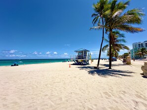 Ein Strand mit einem Rettungsturm, Palmen und blauem Himmel.
