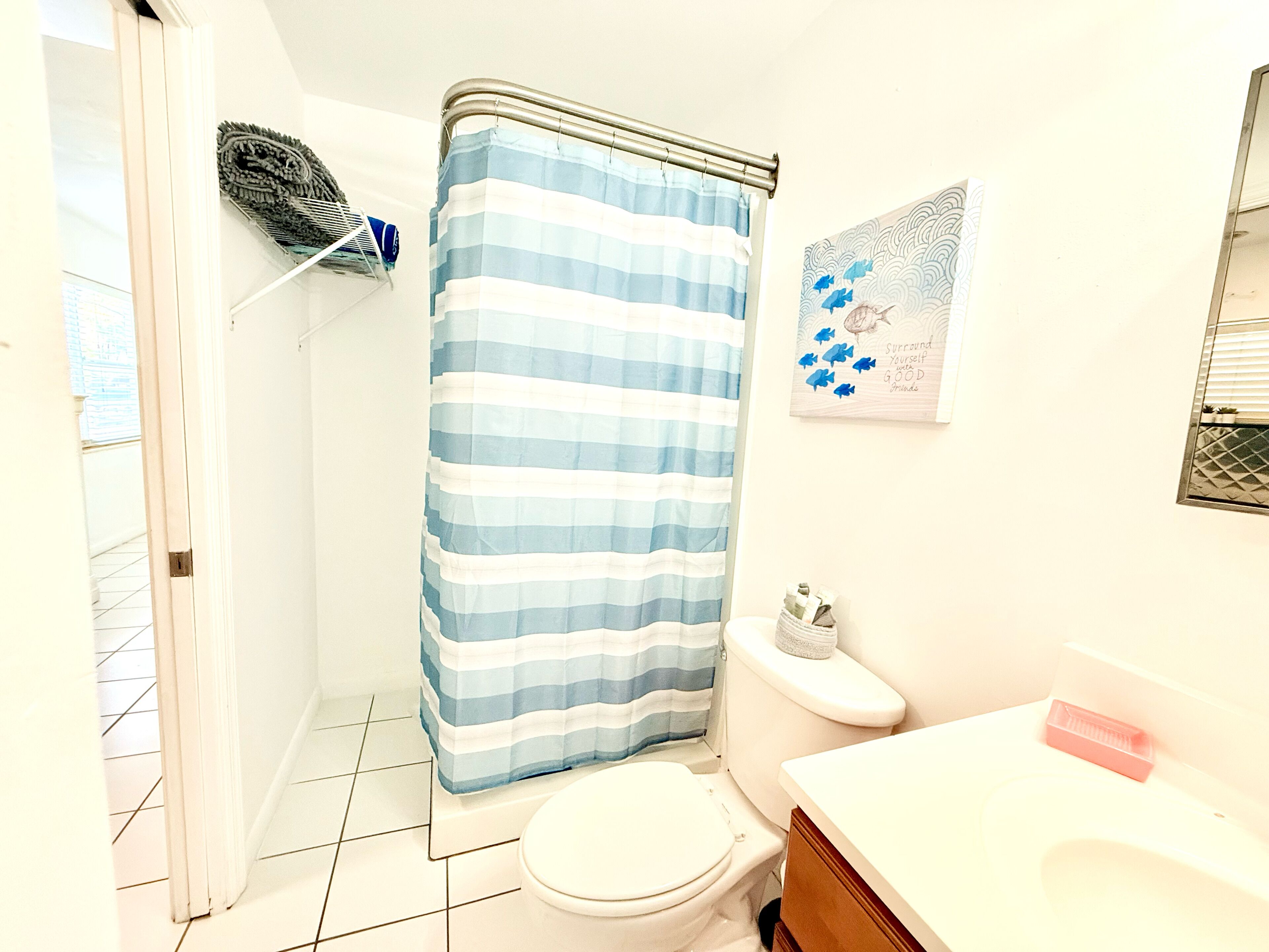 A bathroom with a striped shower curtain, a toilet, a sink with a mirror, and a wall-mounted toilet paper holder.