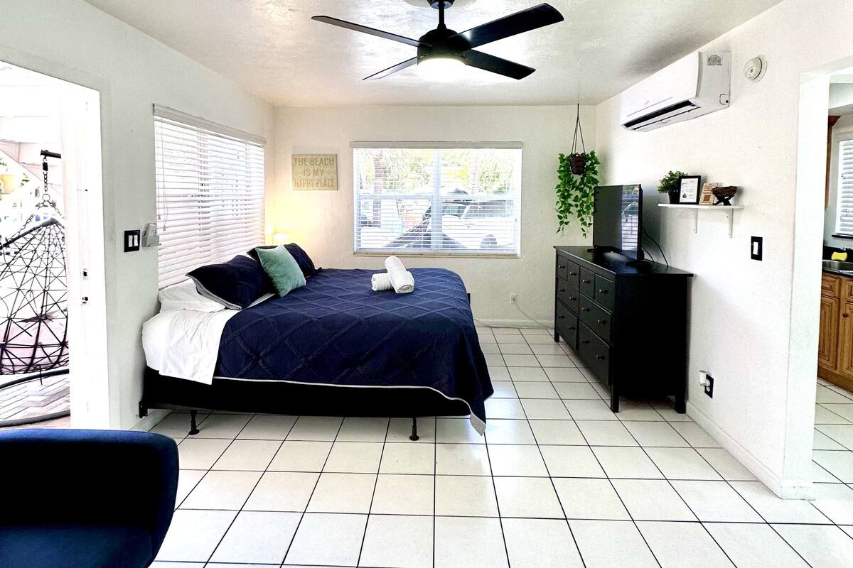 A bedroom with a bed, a ceiling fan, a dresser, a TV, and a window with blinds.