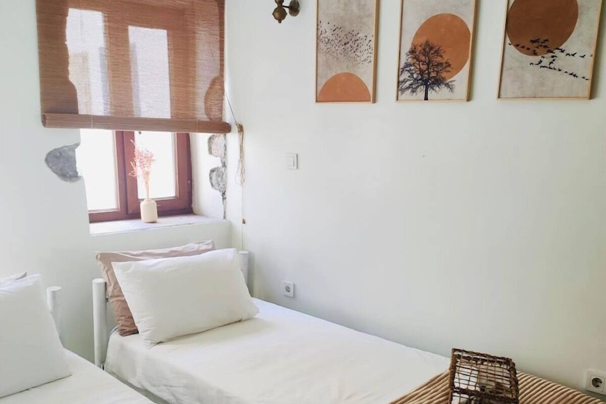 Quarto com duas camas, janela com vista e obras de arte nas paredes.