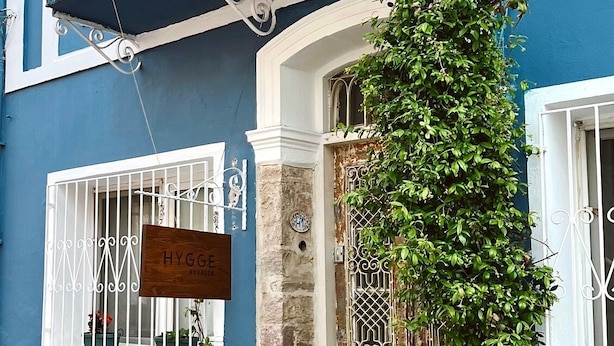 A blue building with a wooden bench and chairs outside, a sign reading "HYGGE AVVÅLK", and a door with a metal gate.