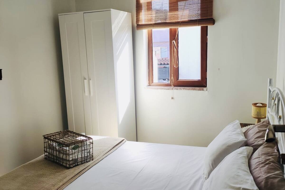 Quarto com cama, guarda-roupa, janela com persianas, ar condicionado e abajur.