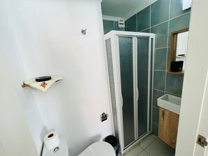 A bathroom with a toilet, a shower enclosure, a sink, and a shelf with toiletries. - Hygge Ayvalık (Ayvalik)