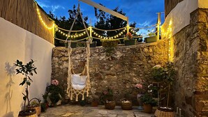 Un patio de piedra con sillas colgantes, luces de cadena y plantas en macetas.