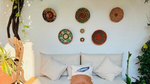 Una cama con ropa blanca, varios almohadones y un cojín decorativo con diseño de plumas.