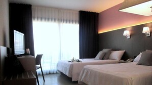 A hotel room with two beds, a desk, a chair, a TV, and a window with curtains. - Fenals Garden (Lloret de Mar)