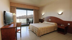 A hotel room with a bed, a desk with a television, a chair, a nightstand, and a view of the outdoors. - Fenals Garden (Lloret de Mar)