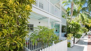 A two-story house with a white picket fence, surrounded by lush greenery and palm trees. - Sago Palm at The Truman Annex in Key West (Key West)