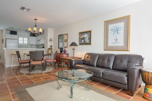 A living room with a glass coffee table, leather sofa, and dining area with chairs and a table.