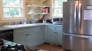 A kitchen with light blue cabinets, a stainless steel refrigerator, a microwave, and a gas stove. - Cozy Cockle Cove Retreat! (South chatham)