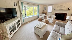 A living room with a television, white furniture, a fireplace, and a large window. - Cozy Cockle Cove Retreat! (South chatham)
