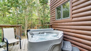 Een houten hut met een bubbelbad op het terras, omringd door bomen.