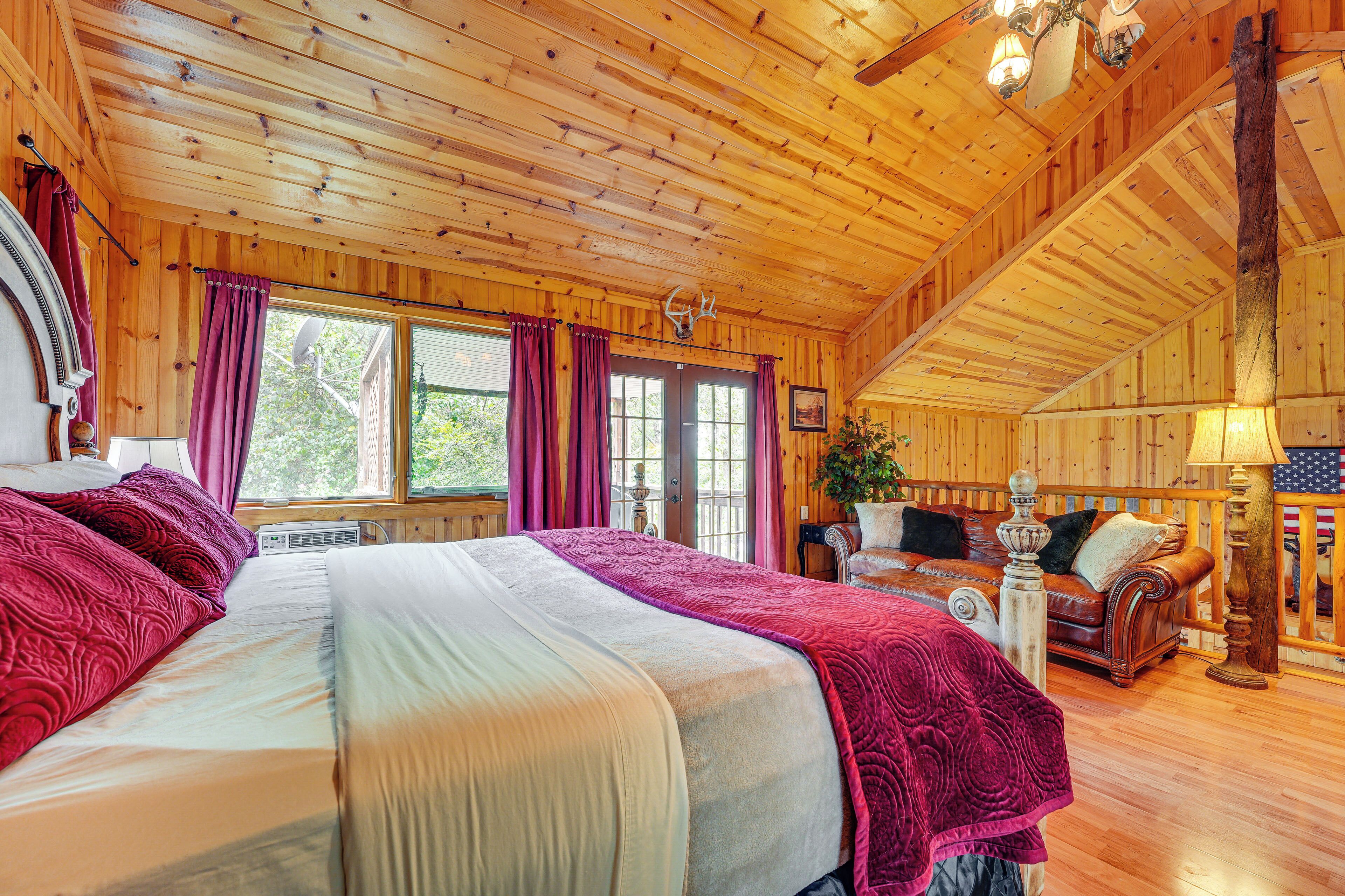 A wooden cabin bedroom with a large bed, a wooden ceiling, and a window with curtains.