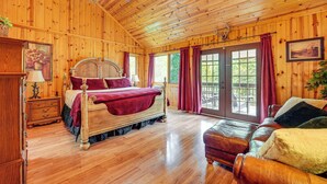 Een houten slaapkamer met een groot bed, een houten dressoir, een leren bank en uitzicht op de natuur via een schuifdeur.