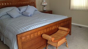A neatly made bed with a wooden headboard, a wicker chair, a bedside table with a lamp, and a framed picture on the wall. - Quiet Waterfront House Sleeps10, Plenty Of Parking, Boat Slip (Rehoboth Beach)