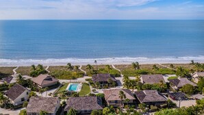 Un complejo turístico costero con varias edificaciones tipo bungalow, una piscina central y vistas al océano.