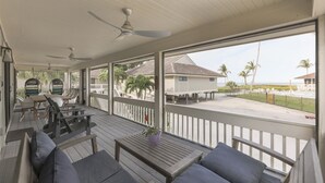 Un espacio al aire libre techado con terraza de madera, asientos y vista a la playa y al océano.