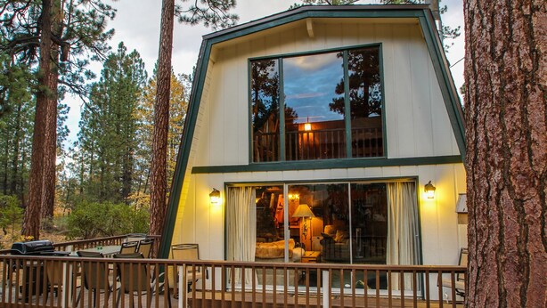 Une cabane à deux étages avec une terrasse, entourée de grands arbres.