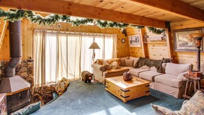 Un intérieur de chalet chaleureux avec une cheminée en pierre, des meubles en bois et une guirlande festive.